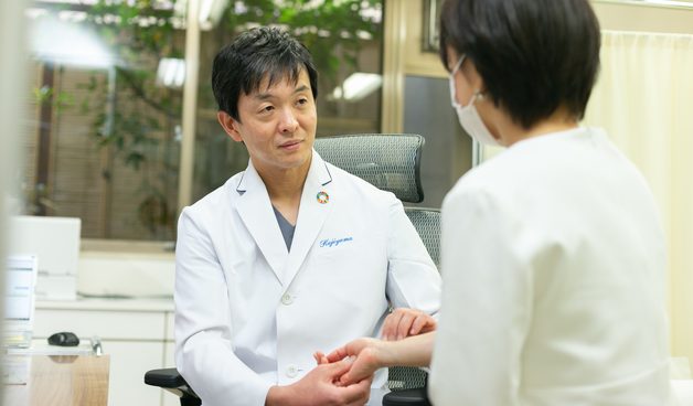 診察室で患者さんの手を取り、話を聞く院長