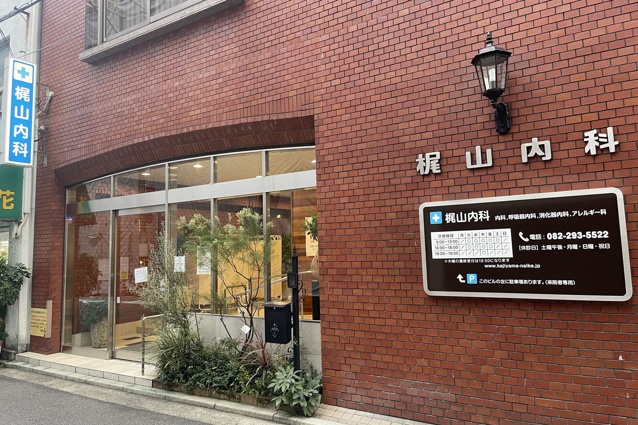 レンガ造りの建物の壁に「梶山内科」の文字と、青い袖看板。1階がガラス張りの入口