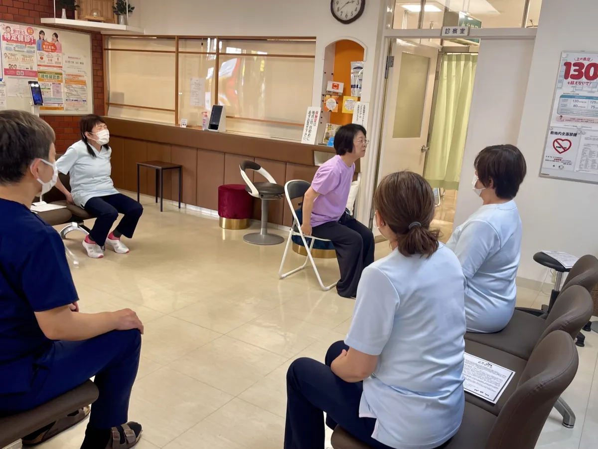 10月22日の教室の様子。待合室に並べた椅子に座ったスタッフが、講師と一緒に体操をしている